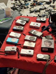 a table topped with lots of cameras on top of a red cloth covered tablecloth