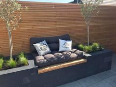 a black couch sitting on top of a wooden bench next to a tree lined fence