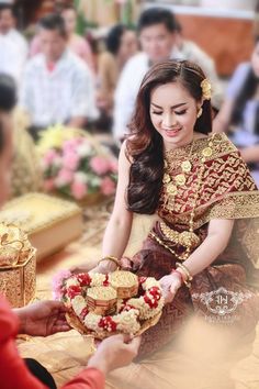 a woman sitting on the floor holding a basket with food in it and another person standing next to her