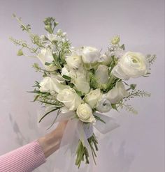 a bouquet of white flowers is being held by a woman's hand in front of a wall