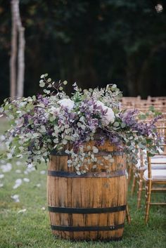 a wooden barrel filled with flowers on top of a grass covered field next to chairs