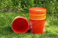 two orange buckets sitting in the grass next to each other