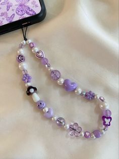 a purple and white beaded necklace next to a cell phone on top of a bed