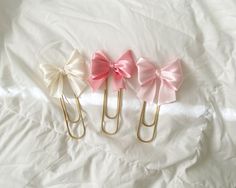 three paper clips with pink bows on them sitting on a white sheet in the bed