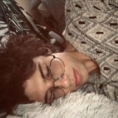 a woman wearing glasses laying on top of a fluffy white blanket next to a plant