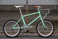 a mint green bike parked next to a fence with a basket on the front wheel