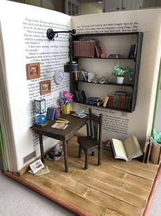 an open book with a miniature table and chair in front of it on a wooden floor