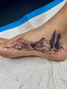 a man's foot with a mountain scene tattoo on the top and bottom of it