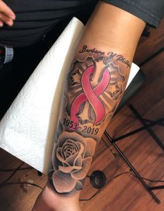 a woman's arm with a rose and ribbon tattoo on it, while she is sitting down