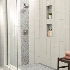 a walk in shower with tiled walls and white tiles on the wall next to a wooden stool