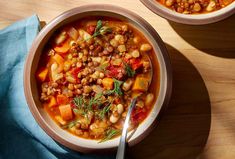 two bowls filled with soup on top of a wooden table next to a blue cloth