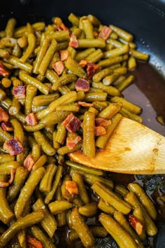 green beans and bacon cooking in a skillet with a wooden spoon on the side