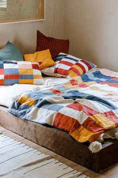 an unmade bed with multicolored blankets and pillows on it in a bedroom