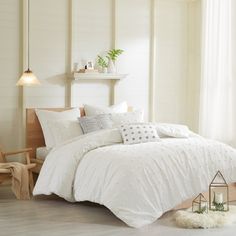 a bed with white comforters and pillows in a room next to a lamp on a table