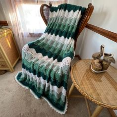 a green and white crocheted blanket sitting on top of a chair next to a table