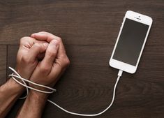 a man is plugging in to an iphone charger on a wooden table with his hands