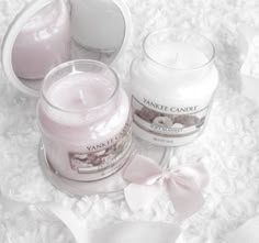 two candles sitting next to each other on top of a white blanket with pink bows