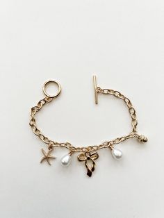 Gold charm bracelet. Charms include pearls, starfish, bow and acorn. Toggle Clasp. Gold Toggle Bracelet, How To Make A Charm Bracelet, Gold Pandora Bracelet, Charm Bracelet Charms, Pearl Charm Bracelet, Gold Girl, Bracelet Charms, Gold Charm Bracelet, Stacked Jewelry