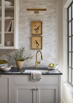 a kitchen with white cabinets and black counter tops, two pictures above the sink that have birds on them