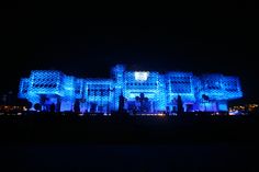 a large building with blue lights on it's sides and people standing outside at night