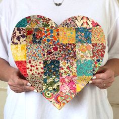 a person holding a heart shaped patchwork piece in their hands and wearing a white t - shirt