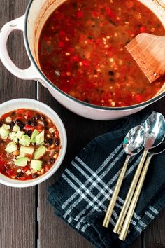 a pot of soup and two spoons on a wooden table next to each other