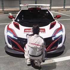 a person sitting in front of a white sports car with red stripes on the hood