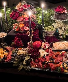 an assortment of fruits and pastries on a buffet table with candles in the background