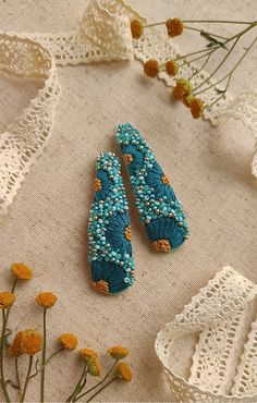 two blue beaded earrings sitting on top of a table next to some yellow flowers