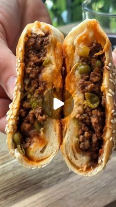 a person holding two sandwiches with meat and cheese on them in front of a table