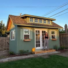 a woman standing in the doorway of a tiny house with windows and sidings on it