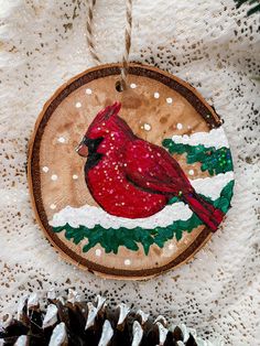 a wooden ornament with a cardinal painted on it and pine cones in the background