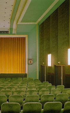 an empty auditorium with rows of green chairs and yellow drapes on the curtained windows