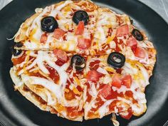 a pizza with olives, tomatoes and cheese on a black plate