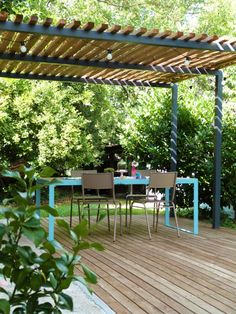 a table and chairs on a wooden deck under a pergolated roof with trees in the background