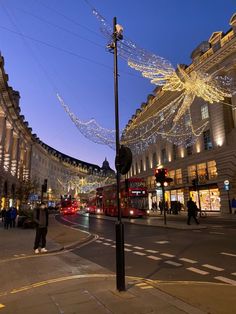 people walking on the street in front of buildings with christmas lights strung across them and decorations hanging from the ceiling