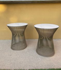 two metal tables sitting next to each other on top of a grass covered ground near a building