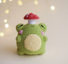 a small crocheted frog with a mushroom on its head sitting in front of a white background