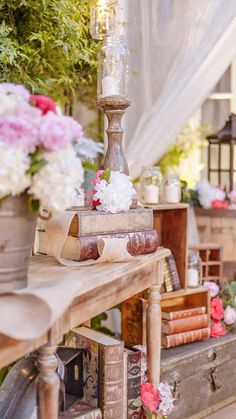 a table topped with lots of books and vases filled with flowers next to a lamp