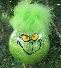 a green ornament with a face painted on it hanging from a pine tree