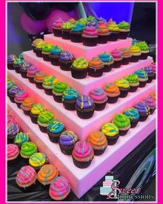 a triple tiered cake with cupcakes on the top and rainbow icing