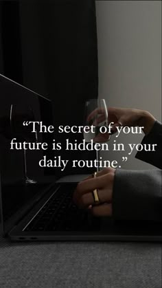 a person holding a wine glass in front of a laptop with a quote about the secret of your future is hidden in your daily routine