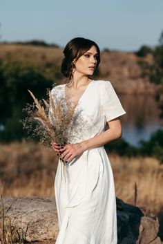 a woman in a white dress holding a bouquet of wildflowers and looking off into the distance