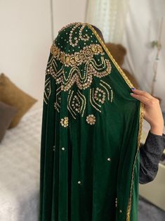 a woman in a green dress is holding up a shawl that has gold sequins on it