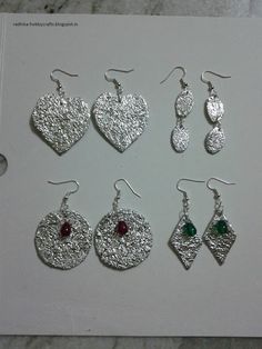 six pairs of earrings are displayed on a white card with red and green stones in them