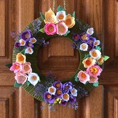 a wreath made out of paper flowers on a wooden door hanger, with purple and pink flowers in the center