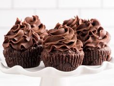 three chocolate cupcakes sitting on top of a white cake plate with frosting