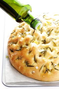 a bottle is being poured on top of a pizza with rosemary sprinkles