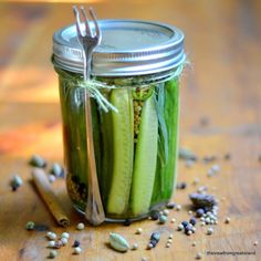 a jar filled with cucumbers and seeds on top of a wooden table next to a fork