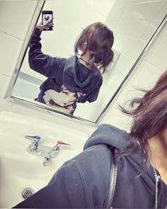 a woman taking a selfie in front of a bathroom mirror with her hair blowing back